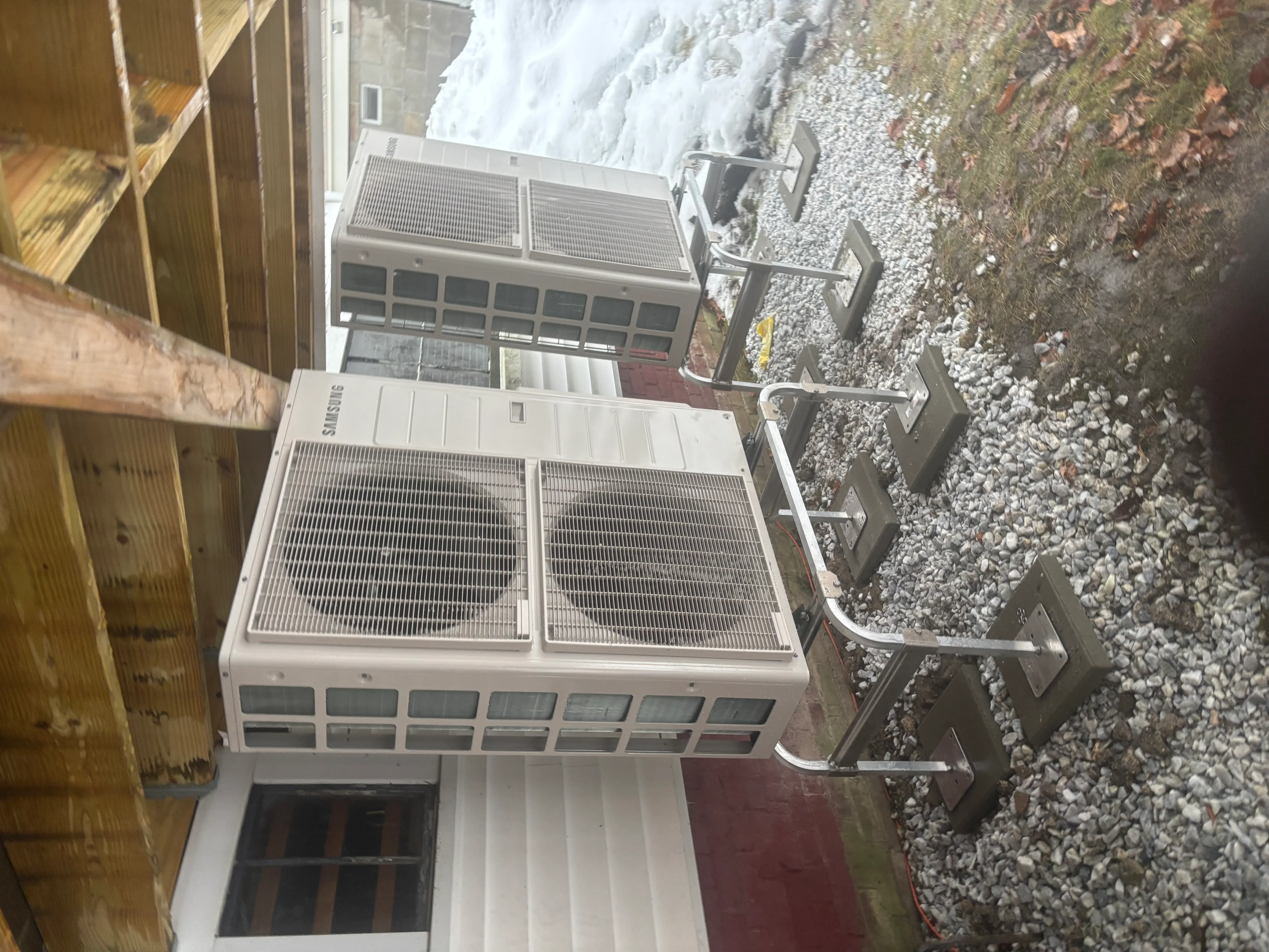 Commercial HVAC condenser units with dual fans and metal mounting brackets on gravel pad