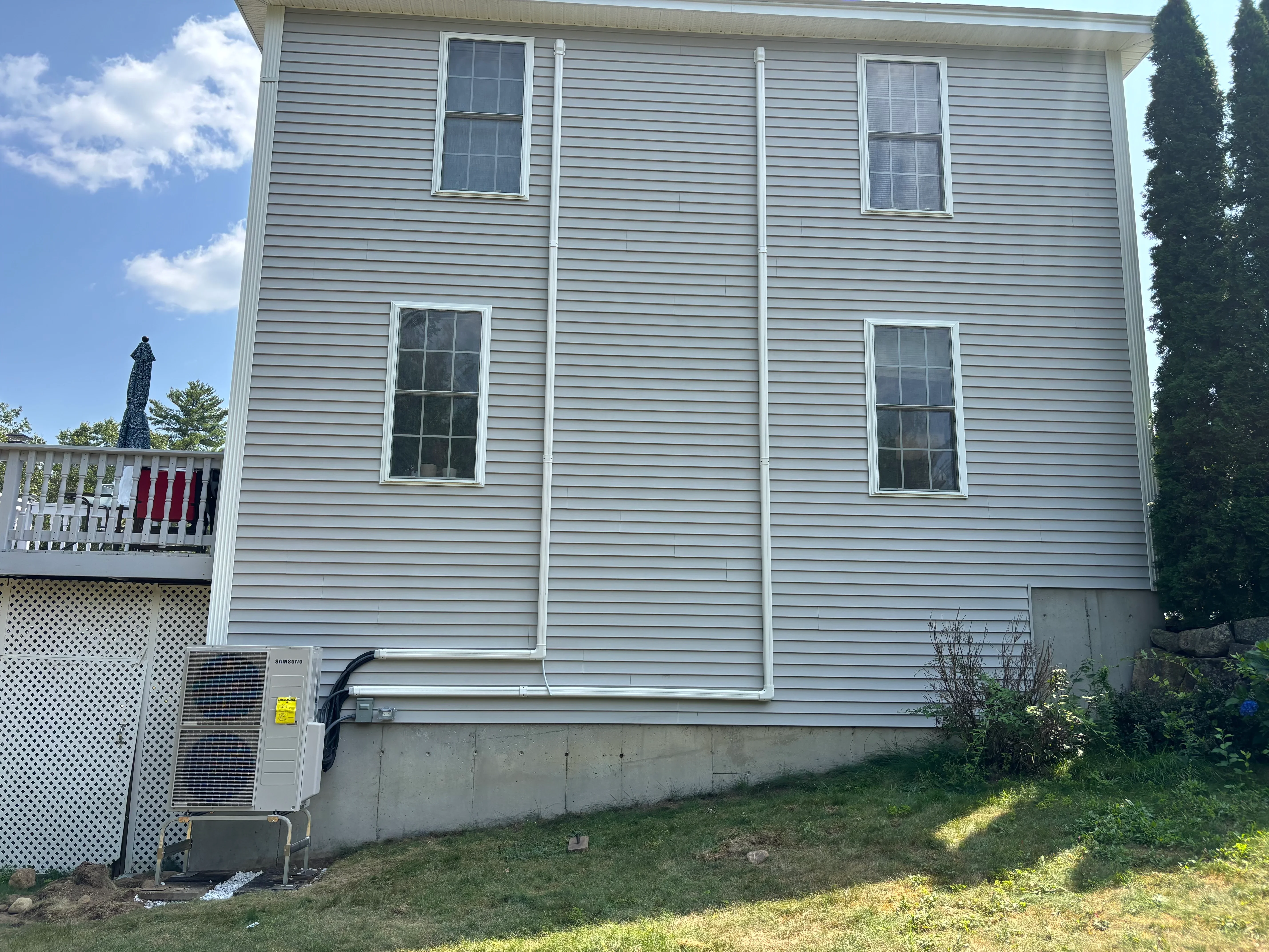 Samsung heat pump unit installed on exterior foundation of gray vinyl-sided home