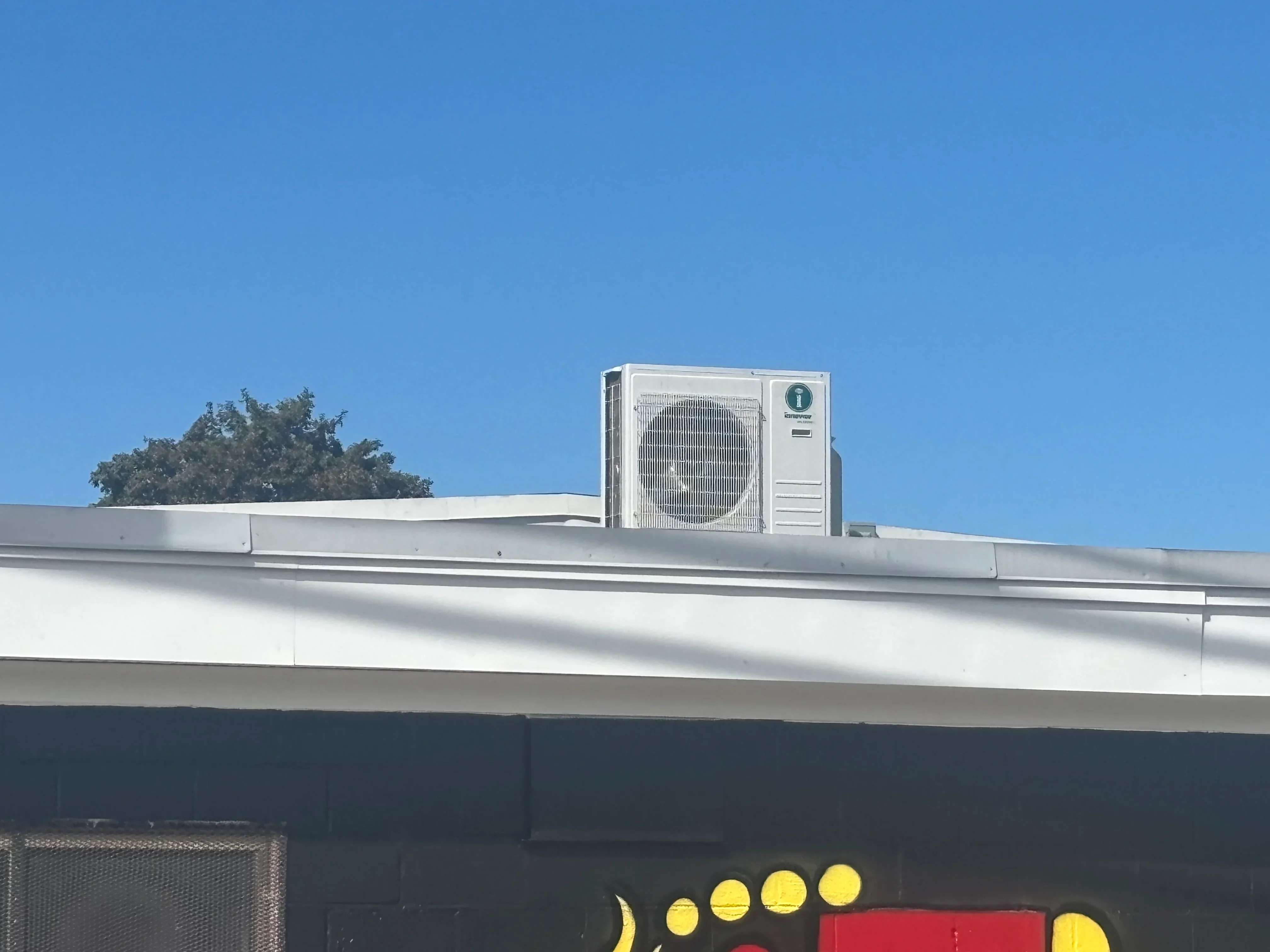White HVAC condenser unit mounted on commercial building roof against clear blue sky